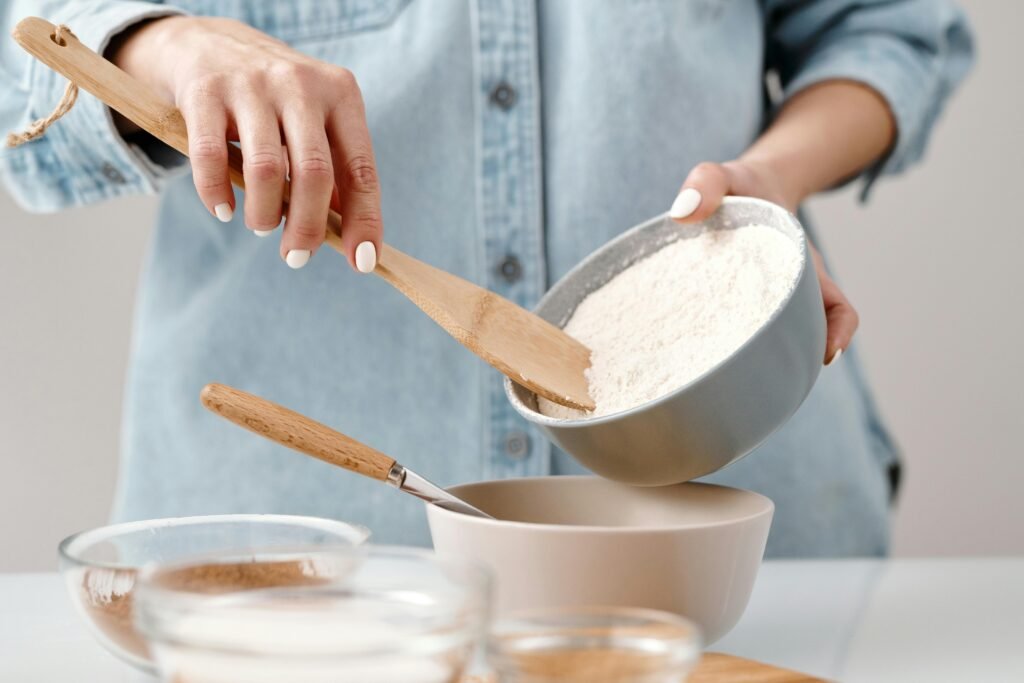 Hands adding flour to a bowl for baking preparation in a kitchen.