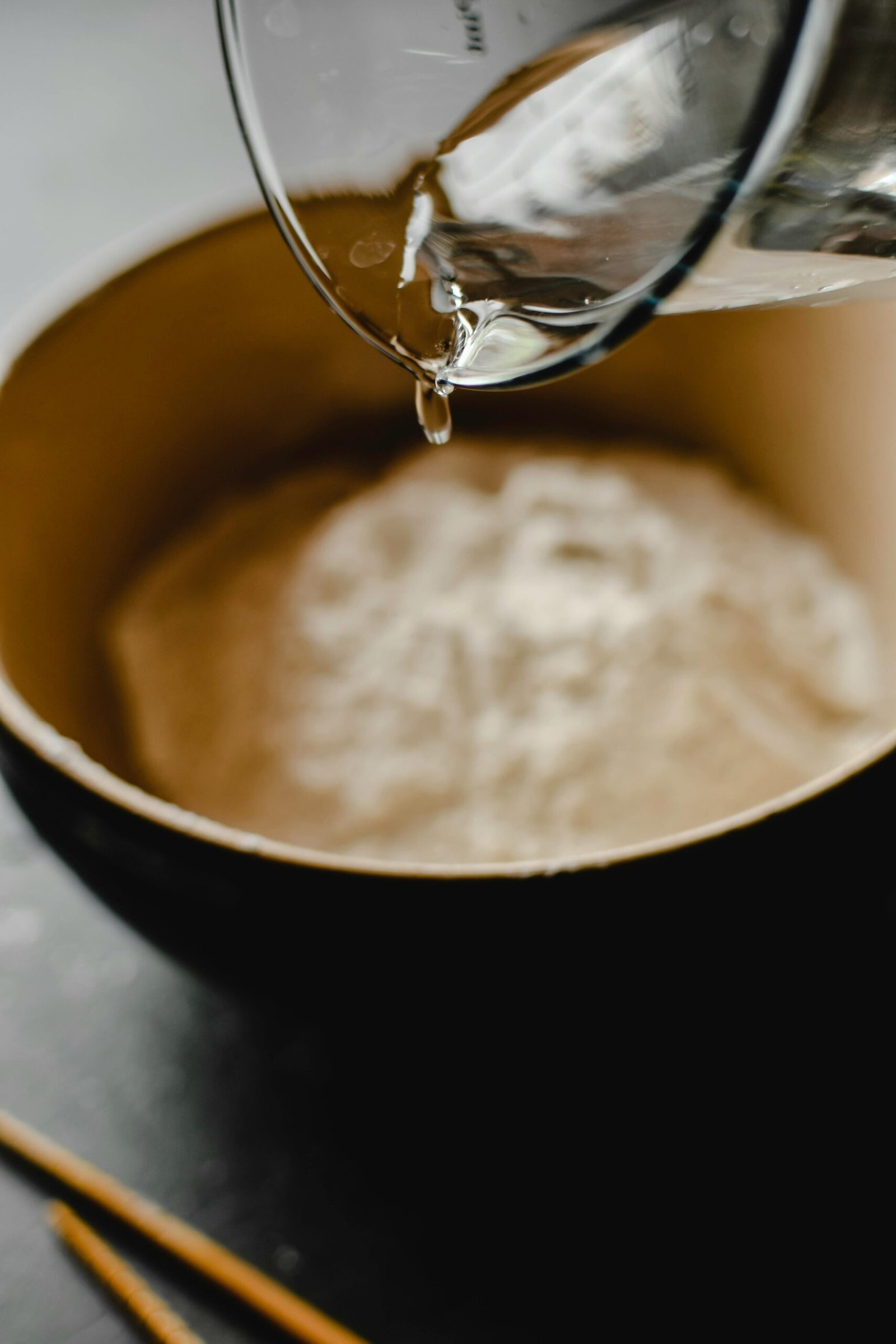 Water being poured into a bowl of flour, focusing on food preparation process.